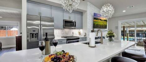 A modern kitchen with a large island, stainless steel appliances, and a chandelier.