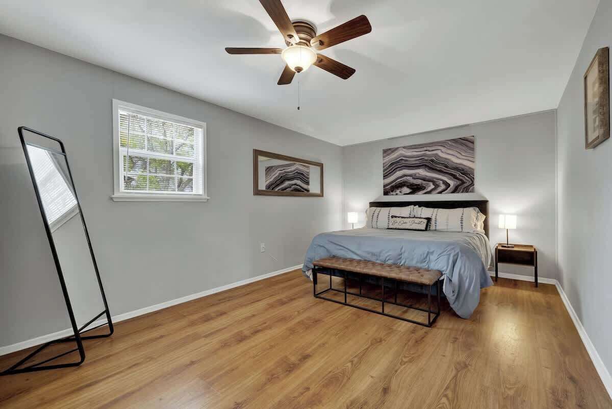 Een slaapkamer met een bed, een plafondventilator, een staande lamp en een groot raam.