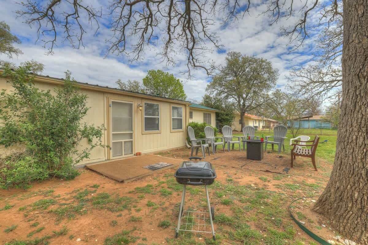 Une maison de plain-pied avec un porche à l’avant, un petit patio aménagé avec du mobilier d’extérieur et un arbre au premier plan.
