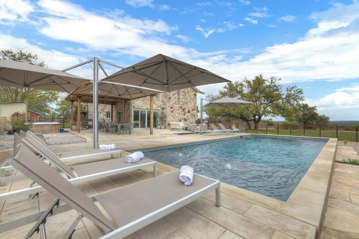 A swimming pool with lounge chairs and umbrellas, a stone building, and a view of the landscape.