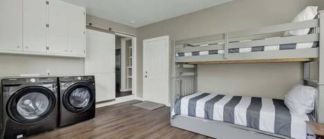 A compact room with a bunk bed, a washing machine, and a door leading to another room.