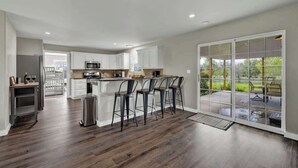 A spacious kitchen with a central island, white cabinetry, and a large sliding glass door leading to an outdoor patio. - River Oaks Retreat With Hot Tub (Fredericksburg)