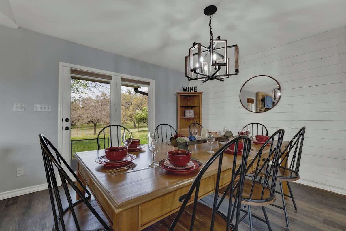 A dining room with a wooden table set for six, black chairs, a chandelier, a wine rack, and a mirror on the wall.