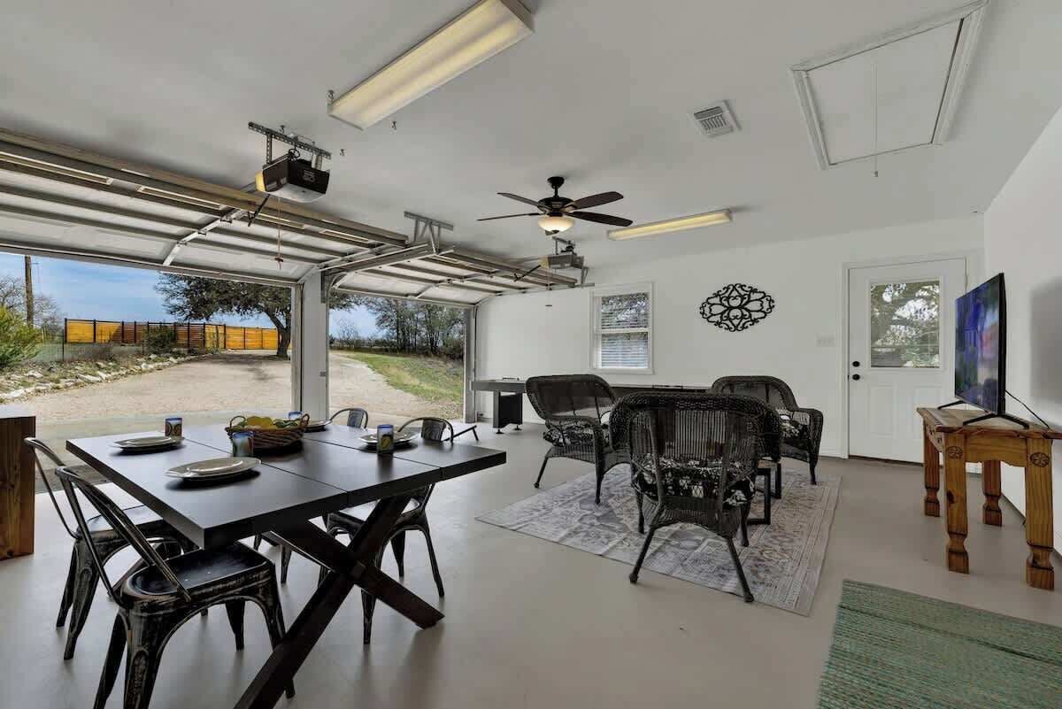 A spacious room with a dining table, chairs, a ceiling fan, and a large window offering a view of the outdoors.
