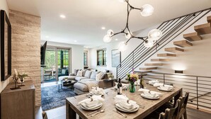 Ein moderner Essbereich mit einem Holztisch, gedeckt für sechs Personen, einer Treppe und einem Wohnzimmer mit Sofa und Couchtisch.