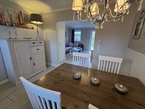 A dining area with a wooden table, white chairs, a chandelier, and a cabinet with drawers. - Torben´s Hüs - Torben´s Hüs, Borgsum (Borgsum)