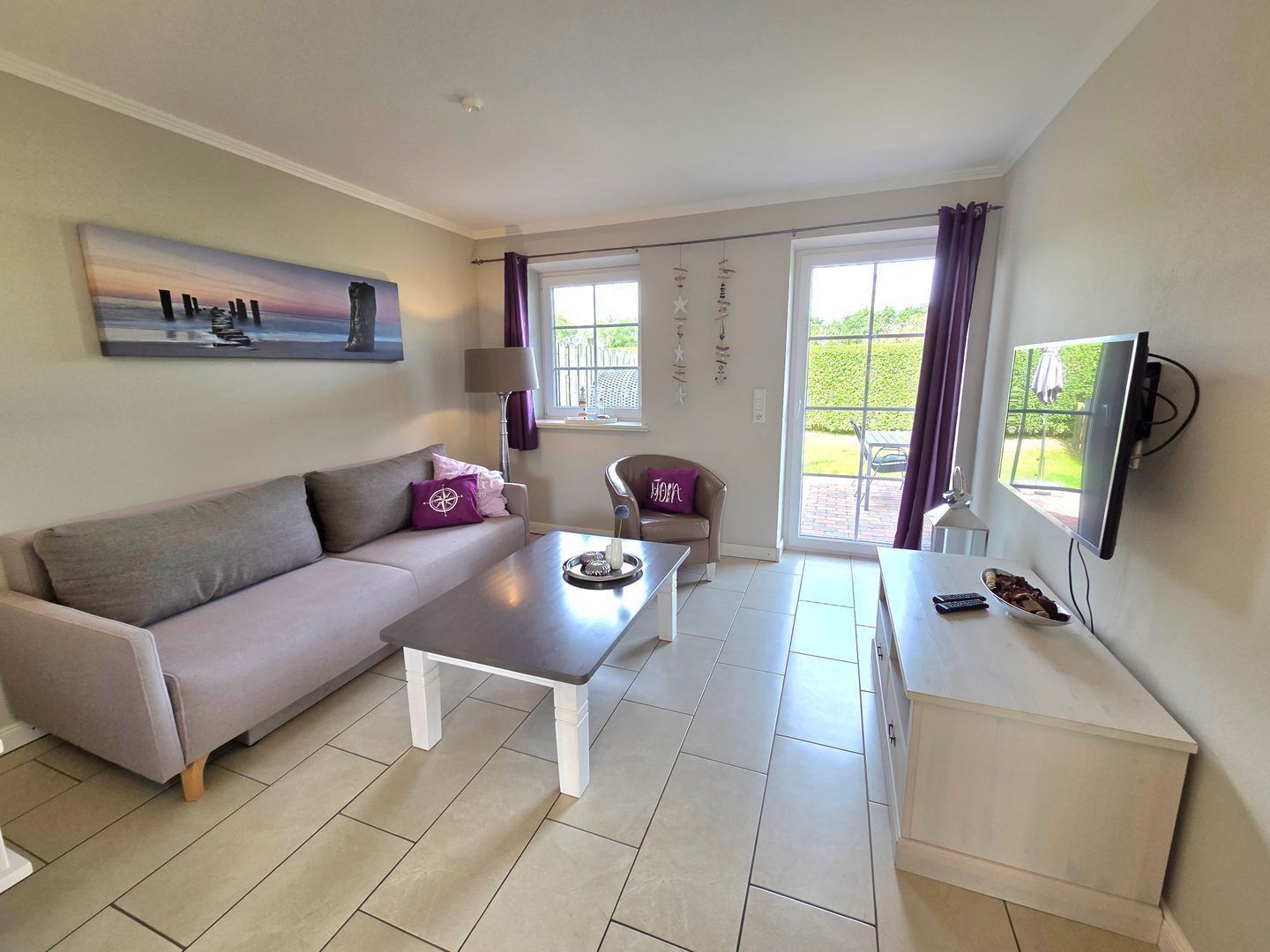 Un salon comprenant un canapé, une table basse, un téléviseur et un balcon avec des rideaux.