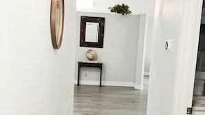 A hallway with a wooden floor, a round mirror, a globe, and a small table with books. - This charming home offers comfort and convenience (Kissimmee)