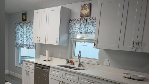 A modern kitchen with white cabinets, a stainless steel sink, and a window with patterned curtains. - This charming home offers comfort and convenience (Kissimmee)