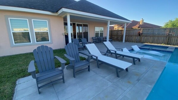 A backyard with a swimming pool, lounge chairs, and a covered patio area.