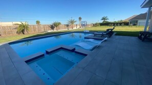 A rectangular swimming pool with a built-in hot tub, surrounded by a tiled patio.