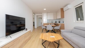 A modern apartment with a flat-screen TV, a wooden coffee table, a grey sofa, and a kitchen with white cabinets and a microwave. - Awesome apartment in Tucepi with WiFi (Tucepi)