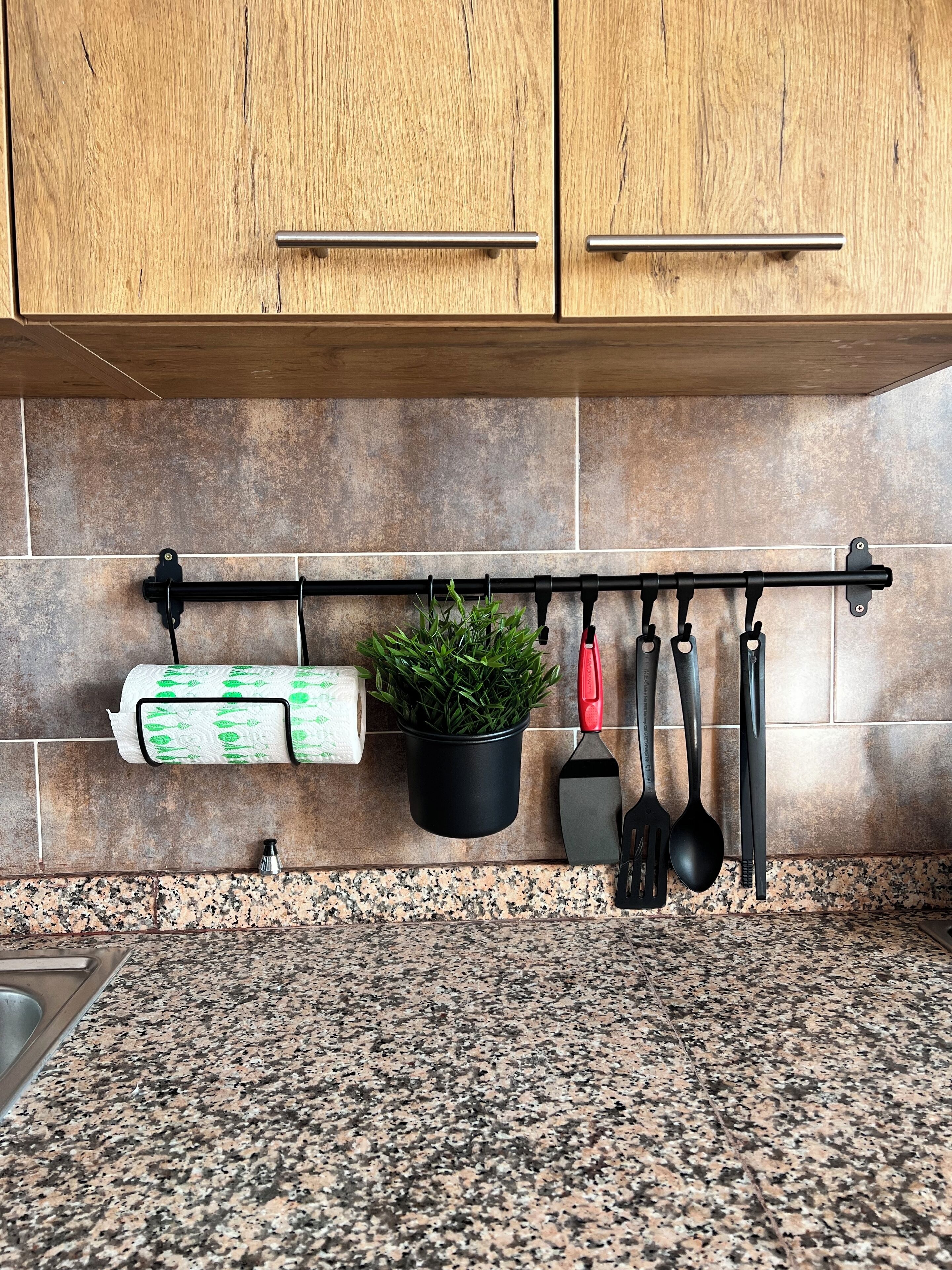 A kitchen with wooden cabinets, a granite countertop, a hanging plant, and kitchen utensils.