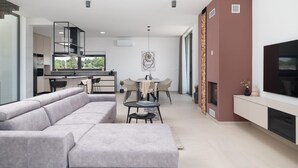 A modern living room with a grey sectional sofa, a dining area with a table and chairs, and a kitchen with a built-in island. - Stunning home in Vrsi with sauna (Vrsi)