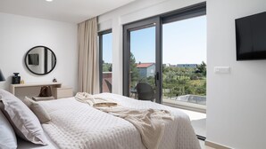 A modern bedroom with a large bed, a round mirror, a bedside table with a lamp, and a TV mounted on the wall. - Stunning home in Vrsi with sauna (Vrsi)