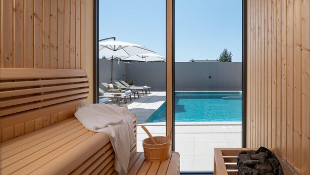 A wooden sauna room with a bench, a wooden bucket, and a view of a pool area with umbrellas and lounge chairs. - Stunning home in Vrsi with sauna (Vrsi)