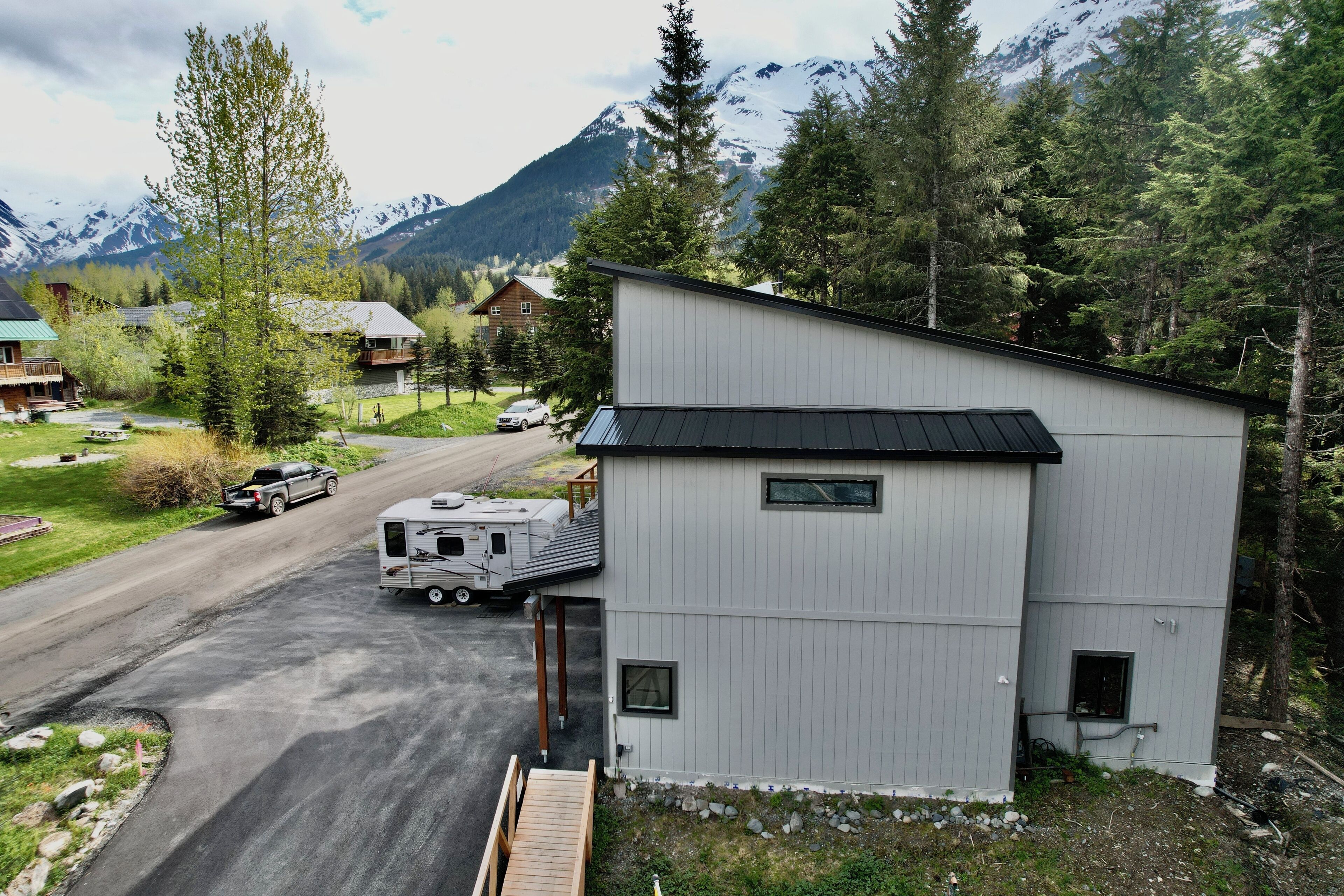 A modern building with a sloped roof, a small porch, and a driveway leading to a parked RV and car.