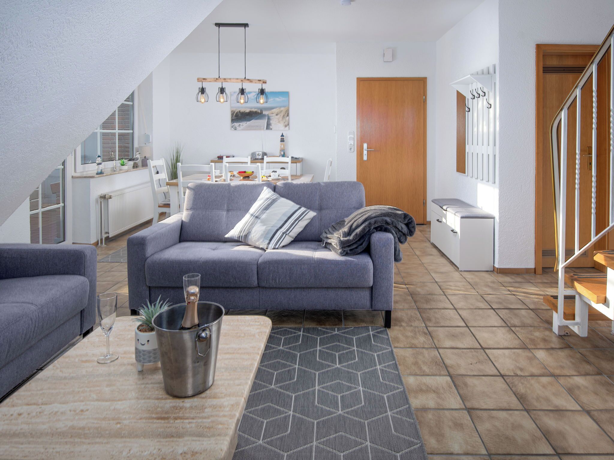A modern living room with a grey sofa, a wooden coffee table, and a dining area in the background.