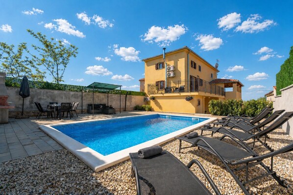 A swimming pool with lounge chairs, a table, and chairs, surrounded by a building with a balcony.