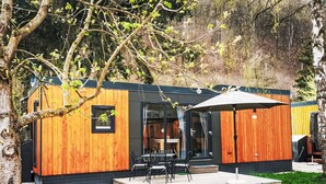 A modern wooden cabin with a patio, outdoor seating, and a large umbrella.