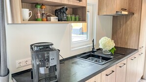 A modern kitchen with wooden cabinets, a black countertop, a coffee machine, a sink, and a window with a view.
