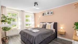 Et soveværelse med en seng, et natbord med lampe, et vindue med gardiner og en radiator.