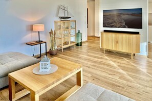 A modern living room with a wooden coffee table, a sofa, a TV mounted on the wall, and a cabinet with glass doors.