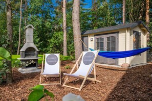 A small outdoor seating area with two lounge chairs and a barbecue grill, surrounded by trees.