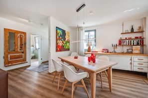 A modern kitchen with a wooden dining table, white chairs, and a colorful abstract painting on the wall.