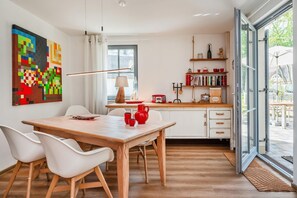 A modern kitchen with a dining area, featuring a wooden table, white chairs, and a large window. - Ferienhaus Auszeitfischer - Neu Errichtetes Ferienhaus in Ruhiger Wohngegend mit Parkplatz, Sauna (Zirchow)