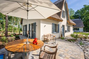 A patio with a round wooden table, two wooden chairs, a red pitcher, and a white umbrella. - Ferienhaus Auszeitfischer - Neu Errichtetes Ferienhaus in Ruhiger Wohngegend mit Parkplatz, Sauna (Zirchow)