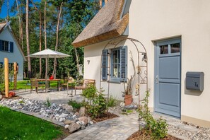Una casa con tejado de paja, un camino de piedra y un pequeño jardín con una mesa y sillas.