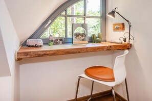 A workspace with a wooden desk, a white chair, a lamp, and a window with a view of trees.