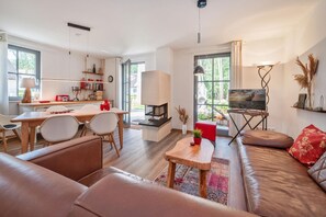 A modern living room with a sofa, a dining area with chairs, a TV, and a fireplace. - Ferienhaus Auszeitfischer - Neu Errichtetes Ferienhaus in Ruhiger Wohngegend mit Parkplatz, Sauna (Zirchow)