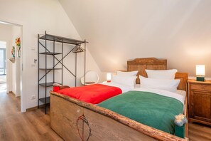 A bedroom with a wooden bed, a metal wardrobe, a white chair, and a bedside table with a lamp.