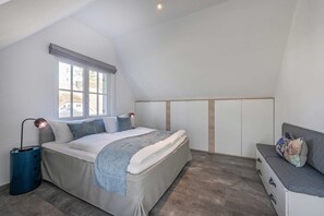 Un dormitorio con cama, mesitas de noche, una ventana y un banco empotrado.