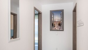 Un couloir avec un plancher en bois, une porte donnant sur une autre pièce et un tableau représentant une scène de plage, accroché au mur.