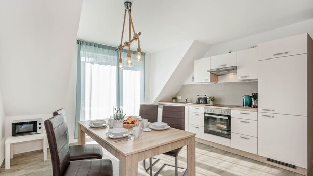 Une cuisine moderne avec un coin repas, comprenant une table en bois, des chaises et un luminaire original.