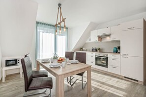 A modern kitchen with a dining area, featuring a wooden table, chairs, and a unique light fixture. - Ferienhaus Himmelblau OG - Entspannte Auszeit: Fewo in Loddin für 4 Gäste (Loddin)