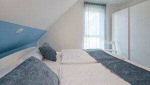 Une chambre avec deux lits, une fenêtre avec des rideaux légers et une chaise blanche.