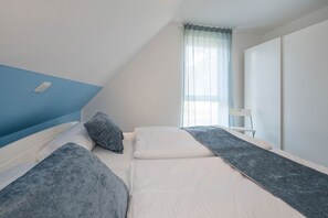 Een slaapkamer met twee bedden, een raam met dunne gordijnen en een witte stoel.