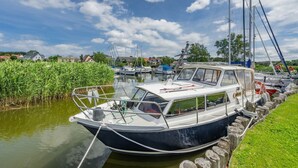 Un étroit canal où une barque est amarrée au bord, entouré de verdure et avec des maisons en arrière-plan.