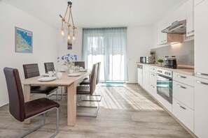 Een moderne keuken met witte kasten, roestvrijstalen apparatuur en een eethoek met een houten tafel en stoelen.