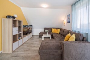 Een moderne woonkamer met een bruine bank, een televisie op een houten kast en een raam met gordijnen.