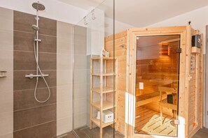 A modern bathroom with a shower, a glass partition, and a wooden sauna.