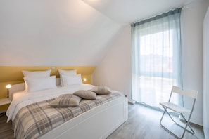 A bedroom with a bed, pillows, a chair, and a window with curtains.