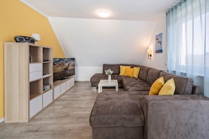 Una sala de estar moderna con un sofá marrón, un televisor sobre un mueble de madera y una ventana con cortinas.