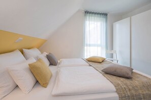 Habitación de hotel con una cama, almohadas, una silla y un ventanal con cortinas.