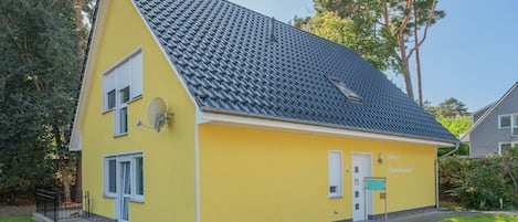 A yellow two-story house with a sloped roof, a satellite dish, and a small porch.