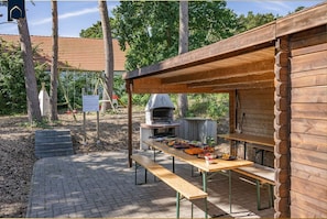 Una estructura de madera al aire libre con un patio de ladrillo, una parrilla y una mesa de picnic.